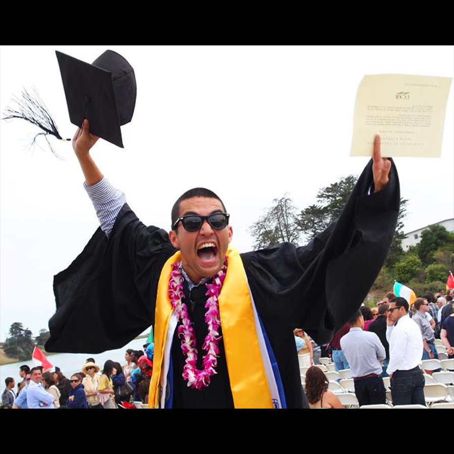 After graduation a college grad cheers excitedly waving his cap and diploma above his head.
