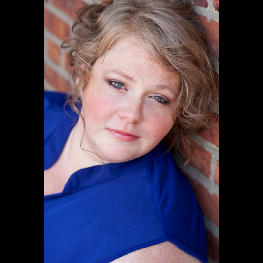 Headshot of woman in blue leaning against a brick wall