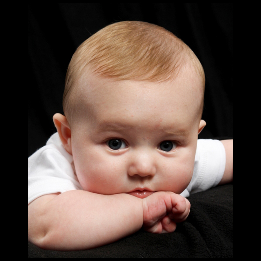 Baby laying down with his chin propped up on his arm.