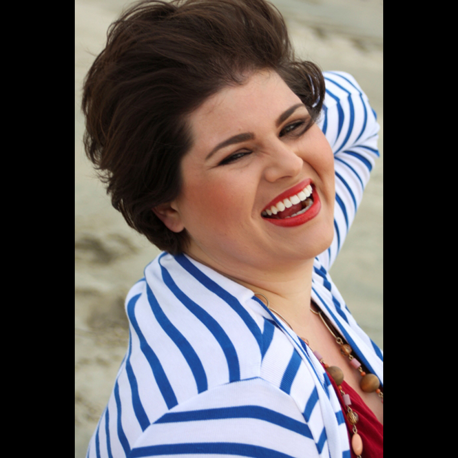 Close up of a woman at the beach in a blue and white stripped shirt who's turn backed towards the camera and laughing.