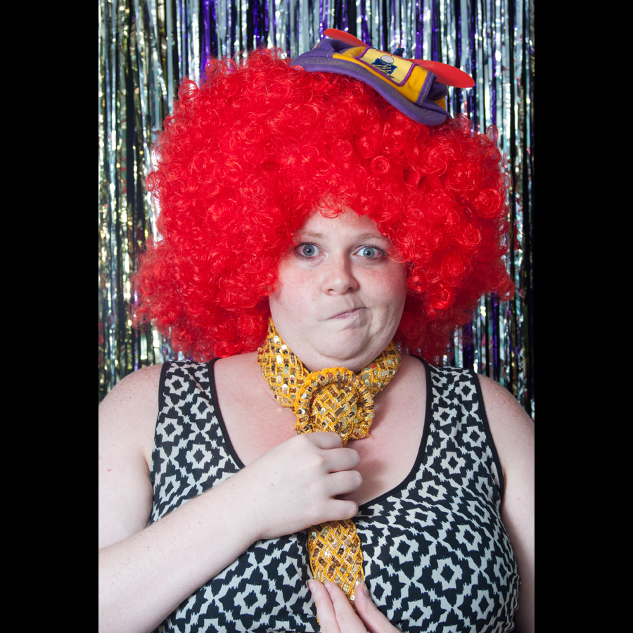 Woman in a big bright red wig and giant gold tie.