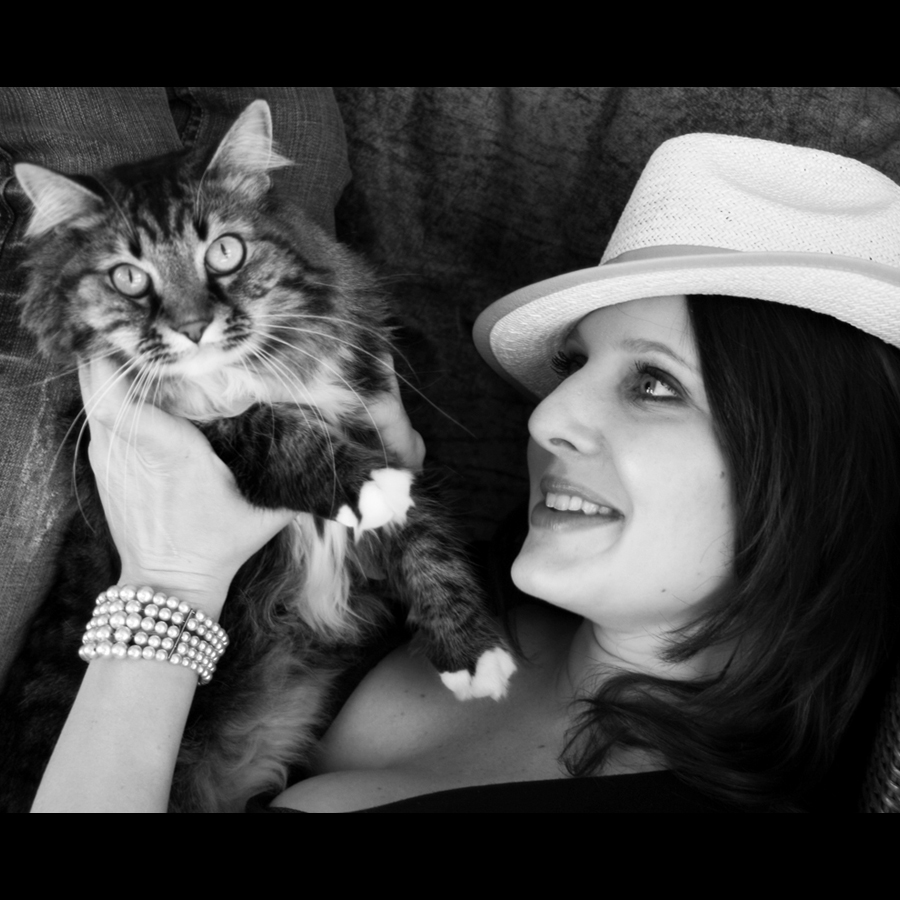 Black and white pitcure of a close up of a woman holding up her long haired tabby cat in from of her and it is looking at the camera