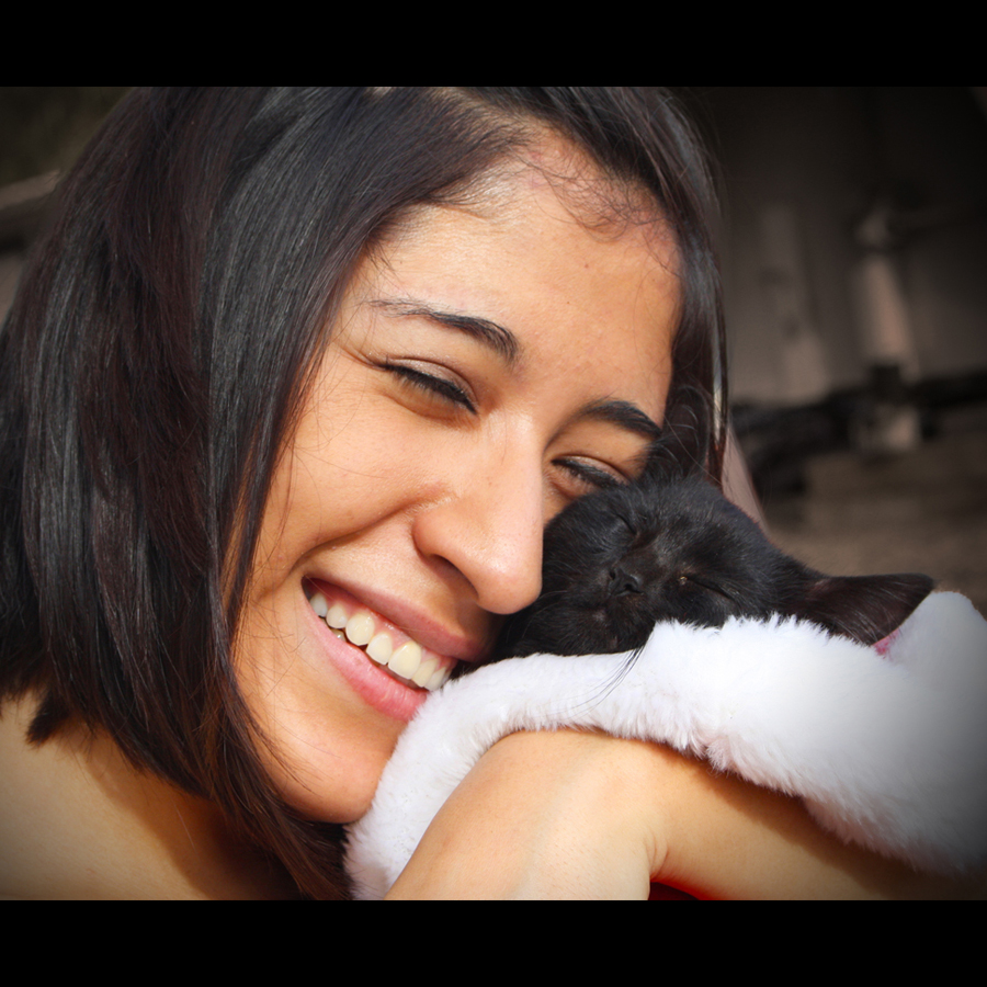 A woman hugs a black kitten up to her face. They both have their eyes closed in bliss.