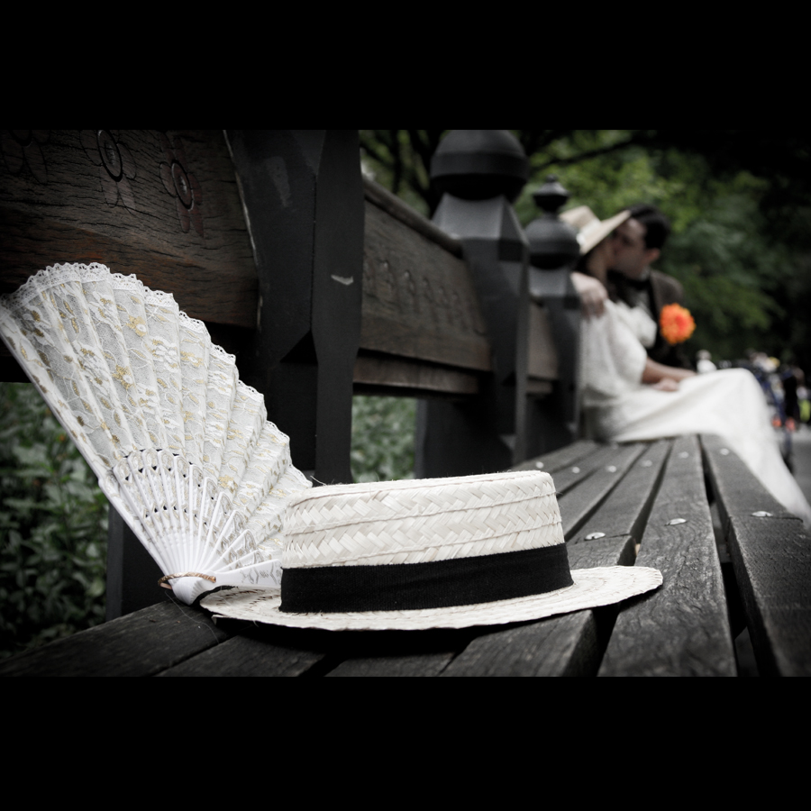 Bride and groom sitting on a bench taking a break, his and hers accessories of a hat and fashion fan await their return.
